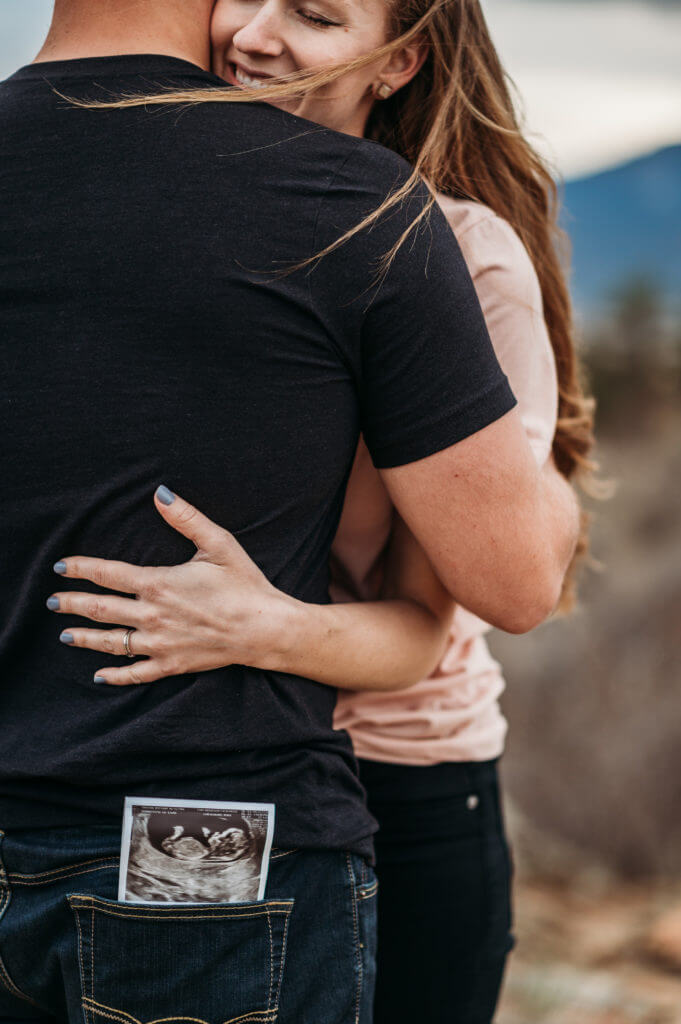 woman hugging man who has ultrasound photo in his back pocket