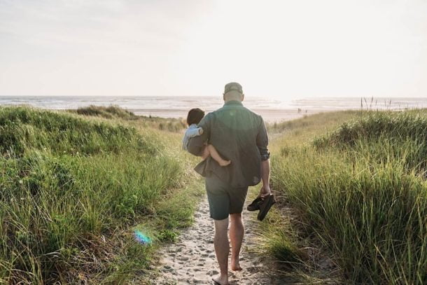father holding daughter walking toward ocean