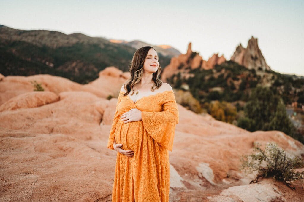 pregnant women at garden of the gods standing on rocks with her eyes closed